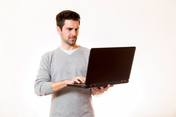 Junger Mann arbeitet im Stehen an einem Laptop den er mit der an Hand haelt