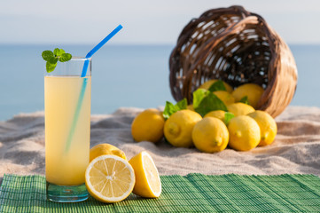 Glass of fresh lemon juice and a full wicker basket with blue sea in the background