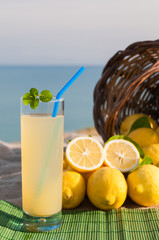 Glass of fresh lemon juice and a full wicker basket with blue sea in the background