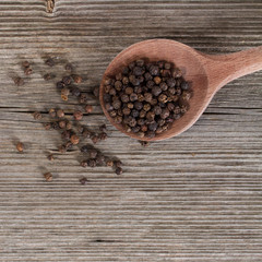whole black pepper on wooden spoon