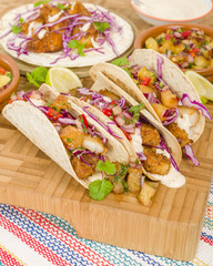Fototapeta premium Baja Fish Tacos - Soft shell tacos filled with seasoned fried white fish served with red cabbage, pineapple salsa, chunky guacamole and creamy Baja style sauce. 