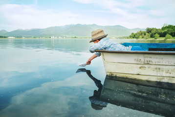Little boy launch paper ship from old boat on the lake
