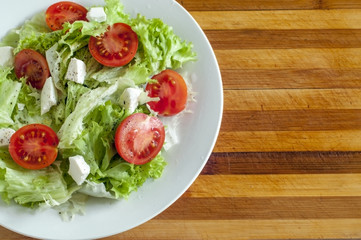 На деревянной доске свежий салат на белой тарелке