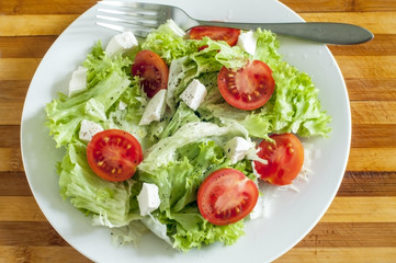 На деревянной доске свежий салат на белой тарелке