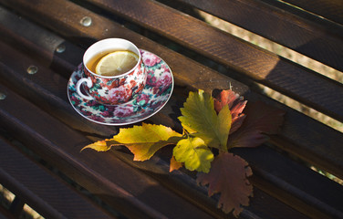 Pink black Cup of tea with lemon on brown wooden bench in autumn Park. 