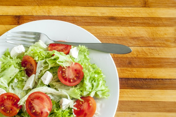 На деревянной доске свежий салат на белой тарелке