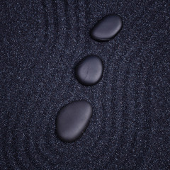 3 black stones aligned in a straight line with waves in a the ze