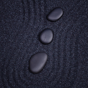 3 black stones aligned in a straight line with waves in a the ze