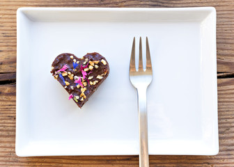 Cute heart shaped piece of chocolate cake sprinkled with flowers