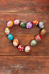 Colourful easter eggs in heart shape on old brown wooden board