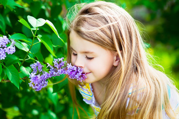 Beautiful blond little girl with long hair smelling flower on sunny day in summer park
