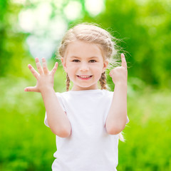 Beautiful blond little girl with two braids  showing six fingers (her age) and smiling on sunny day in summer park