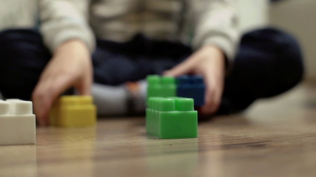Child sitting on the floor and playing with colorful blocks
