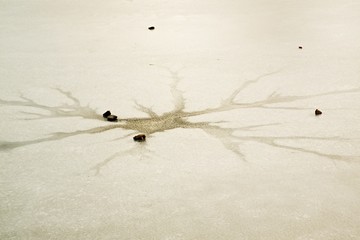 Cracks and hole in ice on pond, dark ice in hole and stone around.