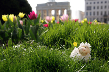 easter in Berlin, toy sheep hiding in green grass with Brandenburger Tor and a fountain