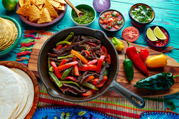 Beef fajitas in a pan sauces chili and sides Mexican
