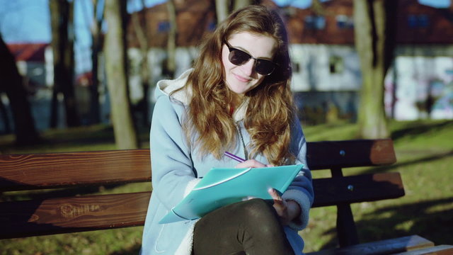 Girl sitting on the bench in the park and writing something
