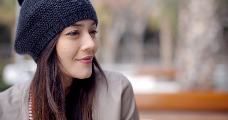 Cute single adult Asian woman in long hair and knitted hat smiling as she looks to the side