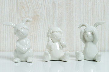 Three funny white ceramic rabbits with helmets out of eggs on a white tile in front of a wooden background