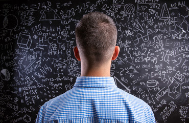 Back view of teacher against big blackboard with mathematical sy
