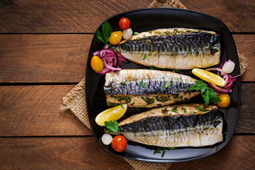 Baked mackerel with herbs and garnished with lemon and pickled vegetables. Top view