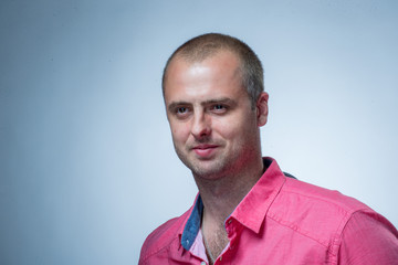 Close up portrait of short-haired brutal man wearing pink shirt on gray background
