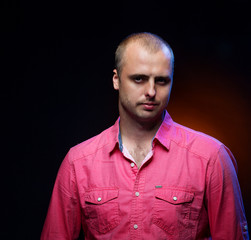 Obraz premium Close up portrait of short-haired brutal man wearing pink shirt on dark background