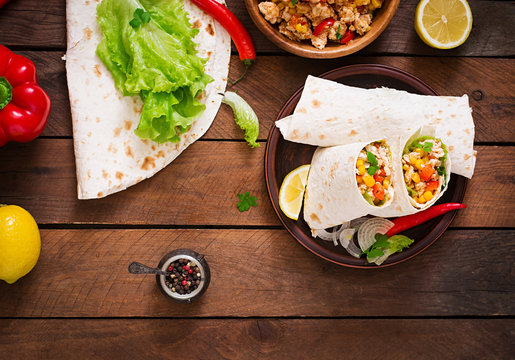 Burritos wraps with chicken meat, corn, tomatoes and peppers on wooden background. Top view