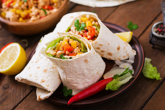 Burritos wraps with chicken meat, corn, tomatoes and peppers on wooden background