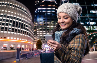 Obraz premium Woman in winter coat with smart phone in night city
