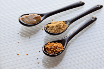 Mustard seeds, mustard powder and mustard sauce in three small spoons