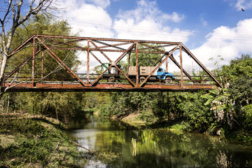 Fototapeta premium Kuba: Alter traditioneller LKW auf rostiger Brücke über ruhigem Fluss in der Mitte der kubanischen Karibik Insel