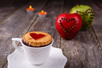 Valentines Day card - Cookies with heart and cup of coffee, candle, apple at old wooden background.