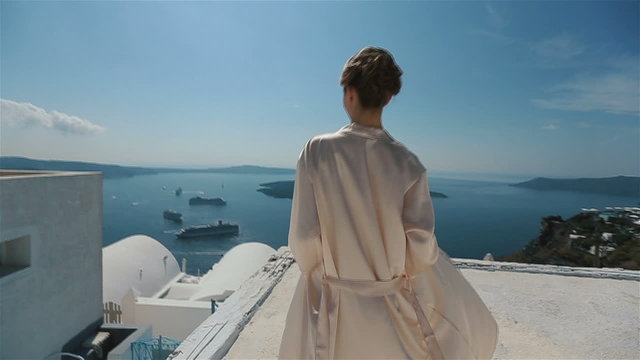 Beautiful sexy brunette bride in robe moving on the roof with sea and mountains in background