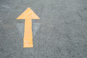 Closeup yellow painted arrow sign on cement street floor background