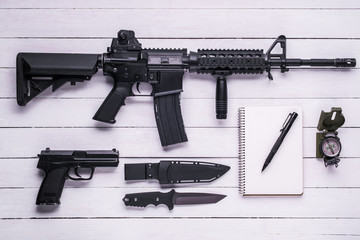 Rifle, gun, knife, compass and notebook on the table/Assault rifle, gun, knife with sheath, compass and notebook with pen on white table.Top view