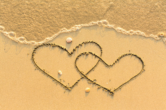 Two hearts drawn on the sand of a beach.