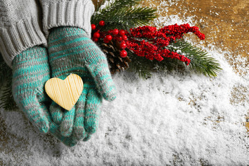 Female hands in blue mittens with decorative heart on snow background