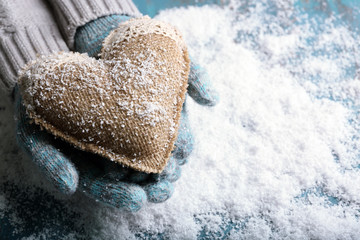 Female hands in mittens with decorative heart on snow background