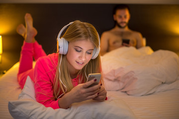 Young women on bed using mobile phone with headphones