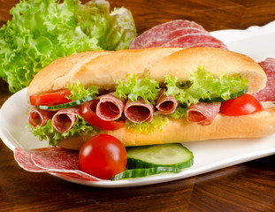 baguette, submarine sandwich, topped with salami, cucumber and t