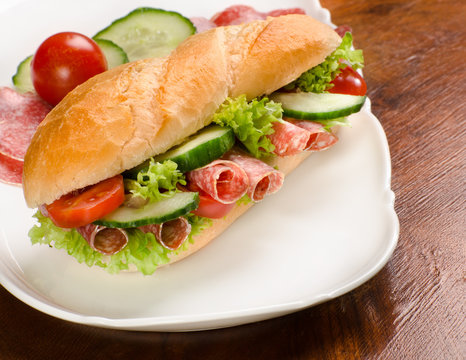 baguette, submarine sandwich, topped with salami, cucumber and t