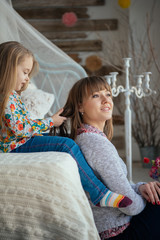 Young cute mother having good time playing with her beautiful daughter in the bed in a big bright room on a sunny day