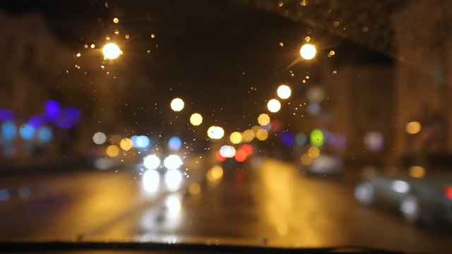 Bad weather, rain and wet snow on the road. Night driving, the road in the headlights of a car window, rain drops and wet snow on the windshield. Bokeh and glare, reflection night lights.