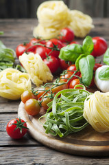 Raw pasta, tomato and basil on the wooden table