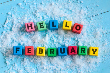 Hello February written on colour wooden toy cubes On light background with snow