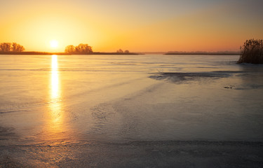 Naklejka premium Winter landscape with frozen lake and sunset fiery sky. 