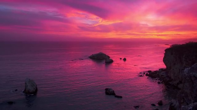 Colorful sunset over ocean cliffs in Pismo Beach, California. Camera tilt down.