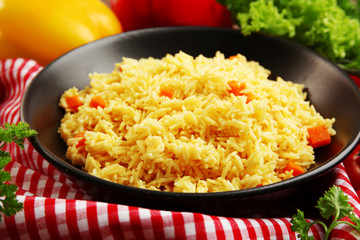 Stewed rice with a carrot on a black plate, close up