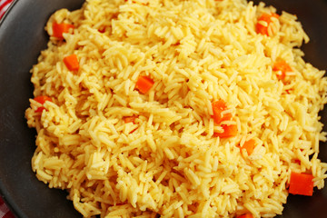 Stewed rice with a carrot on a black plate, close up